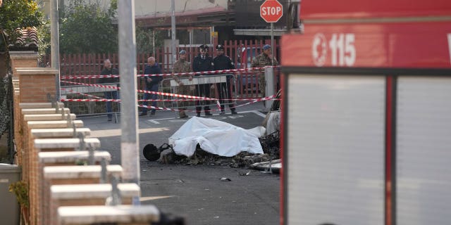 The burned remains of one of the two Italian Air Force U-208 aircrafts that crashed in Guidonia, on the outskirts of Rome, Tuesday, March 7, 2023, is covered with a white cloth in the residential district where it fell. Two pilots died in the crash.