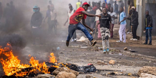 An anti-government protester jumps in the air as he throws a rock towards the police next to a burning barricade in Nairobi, Kenya, on March 20, 2023.
