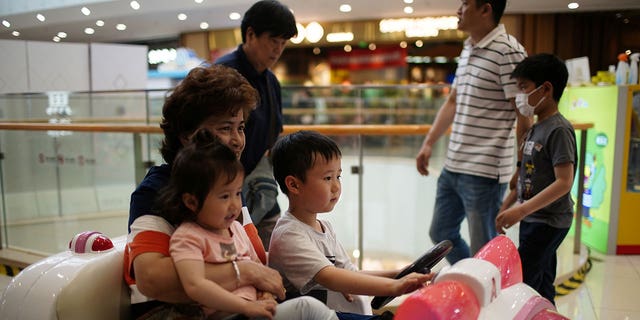 A person holds a girl while a boy drives a toy car at a shopping mall in Shanghai, China, June 1, 2021. 