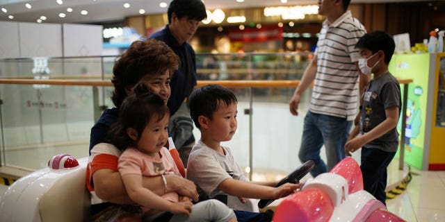 A person holds a girl while a boy drives a toy car at a shopping mall in Shanghai, China, June 1, 2021. 