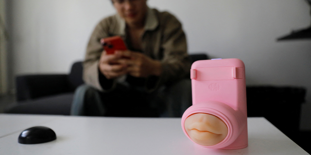 Jing Zhiyuan uses his phone near a remote kissing device "Long Lost Touch," as he demonstrates how to use it during an interview with Reuters, at his home in Beijing March 12, 2023.