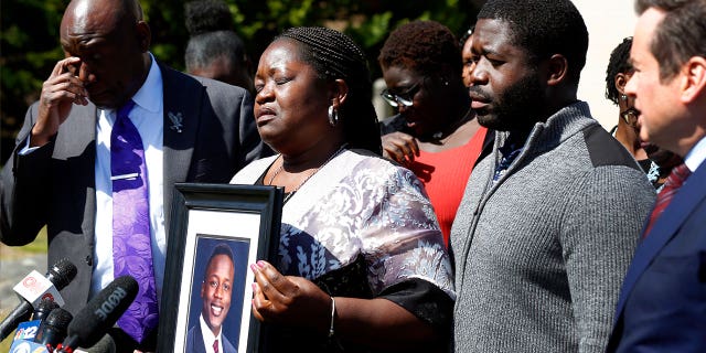 Caroline Ouko, mother of Irvo Otieno, holds a portrait of her son with attorney Ben Crump, left, her older son, Leon Ochieng and attorney Mark Krudys at the Dinwiddie Courthouse in Dinwiddie, Virginia, on March 16, 2023.