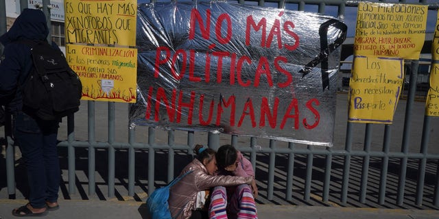 A pair of Venezuelan sisters comfort each other sitting on a sidewalk outside an immigration detention center where dozens of migrants fearing deportation set mattresses ablaze, starting a fire that killed dozens in Ciudad Juarez, Mexico, Tuesday, March 28, 2023. The sign behind the sisters reads in Spanish "No more inhuman policies."