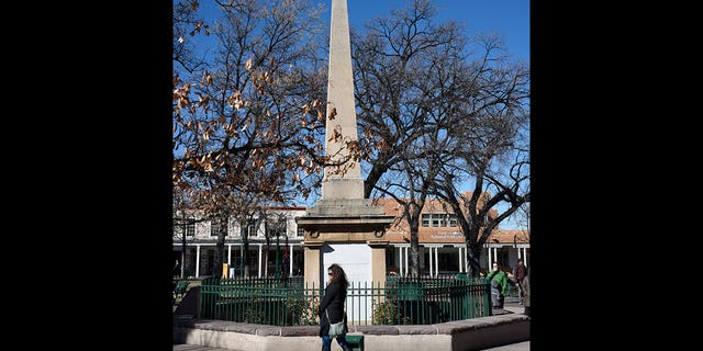 A woman walks past a historic obelisk in the Plaza in Santa Fe, New Mexico, on Nov. 21, 2018. Santa Fe has delayed a plan to rebuild the controversial Civil War obelisk which was destroyed during a 2020 Indigenous rally. The structure was built to dedicate the "heroes" who died while battling against "savage Indians."