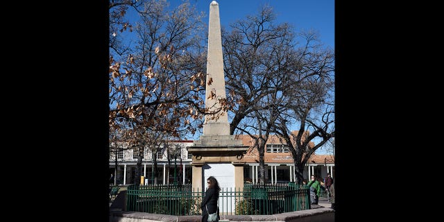 A woman walks past a historic obelisk in the Plaza in Santa Fe, New Mexico, on Nov. 21, 2018. Santa Fe has delayed a plan to rebuild the controversial Civil War obelisk which was destroyed during a 2020 Indigenous rally. The structure was built to dedicate the "heroes" who died while battling against "savage Indians."