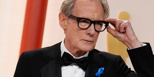 Bill Nighy arrives at the Oscars while wearing a small blue ribbon on March 12, 2023, at the Dolby Theatre in Los Angeles.