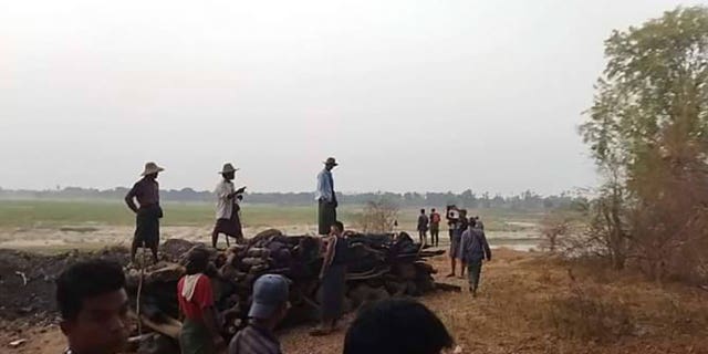 Men stand over a funeral pyre in Tar Taing village as they prepare to cremate bodies of those found dead in Burma on March 2, 2023.