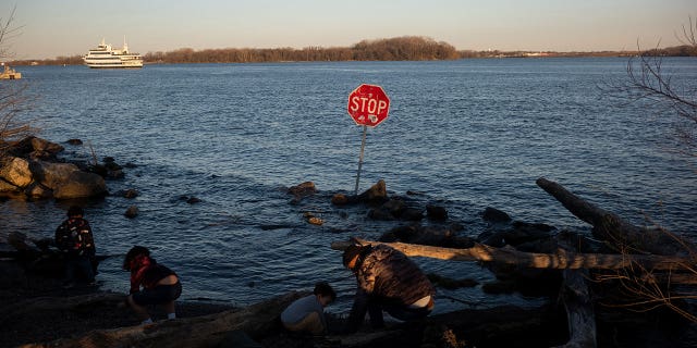 Children play along the Delaware River where a stop sign has been placed in the water at Penn Treaty Park in Philadelphia March 26, 2023.