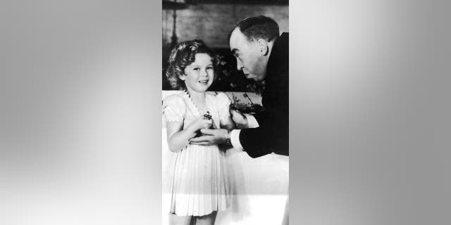 1935: American child actor Shirley Temple receives a special Oscar from American screenwriter Irwin S Cobb (1876 - 1944) at the Academy Awards ceremony, Biltmore Bowl, Biltmore Hotel, Los Angeles, California.