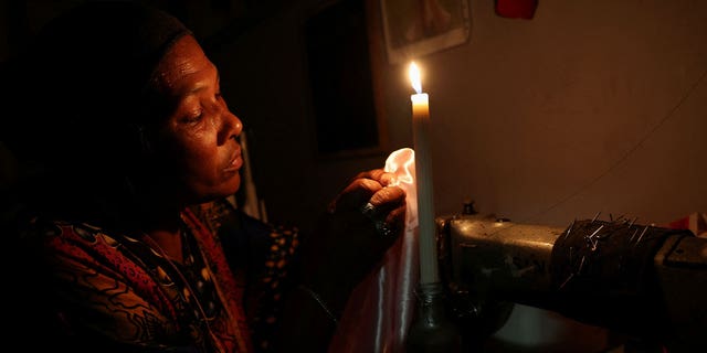 Dressmaker Faieza Caswell sews under candlelight in her workplace as South Africa struggles with power in Cape Town, South Africa, on Feb. 11, 2023. 