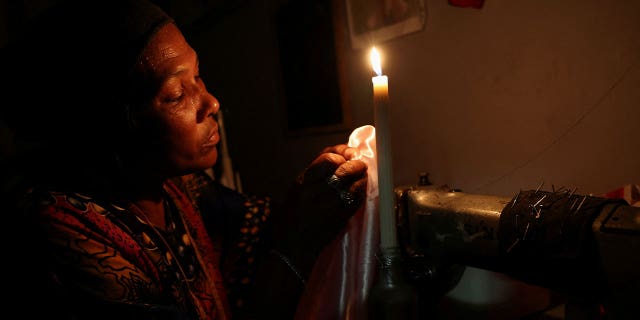Dressmaker Faieza Caswell sews under candlelight in her workplace as South Africa struggles with power in Cape Town, South Africa, on Feb. 11, 2023.