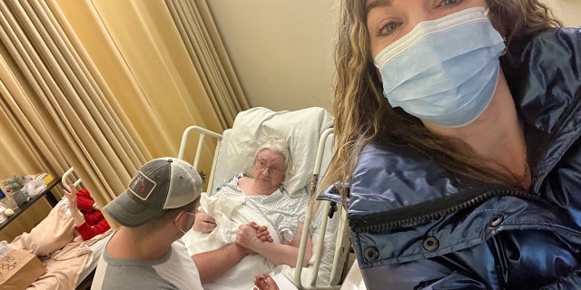 Alice Schuman lies in a hospital bed as Brock Cvijanovich holds her hand. At right, Brock Cvijanovich's mom. The two became Schuman's legal guardians.