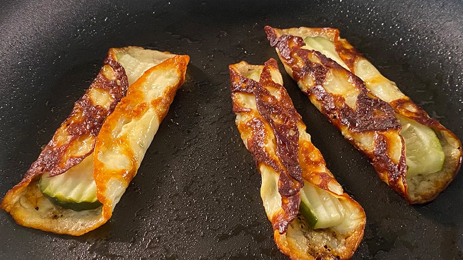Three pickle slices wrapped in provolone cheese on a frying pan