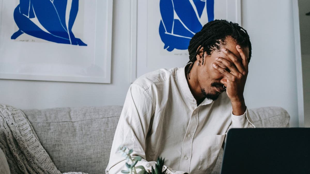 Man sitting on the couch with his hand over his face.