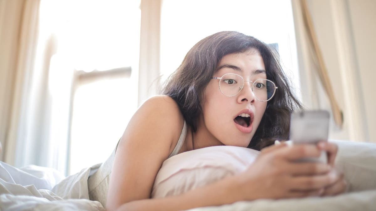 Woman laying down and looking at her phone with a shocked expression.