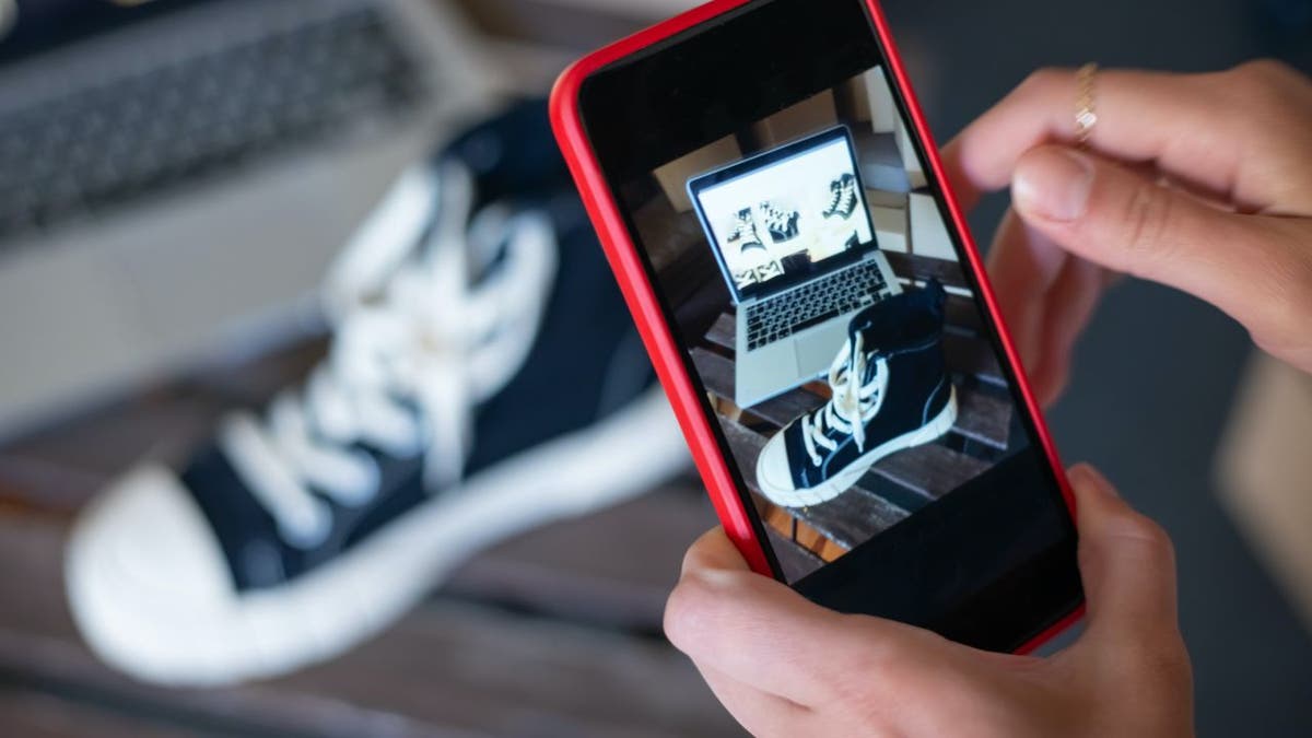 A person holding up a red phone taking a picture of a shoe.