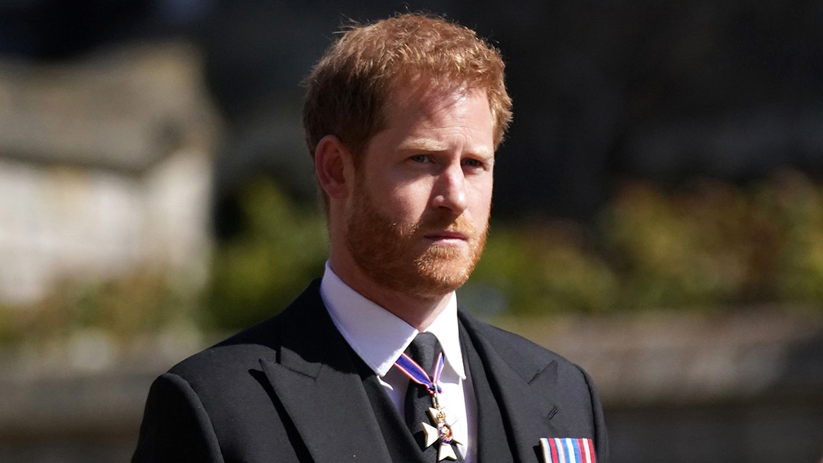 Prince Harry in a suit with medals looking sternly