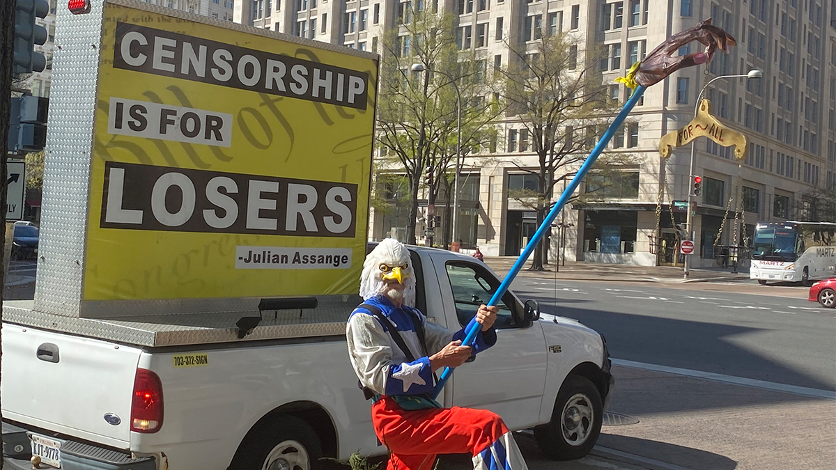Man in eagle costume holding a "peace for all" sign