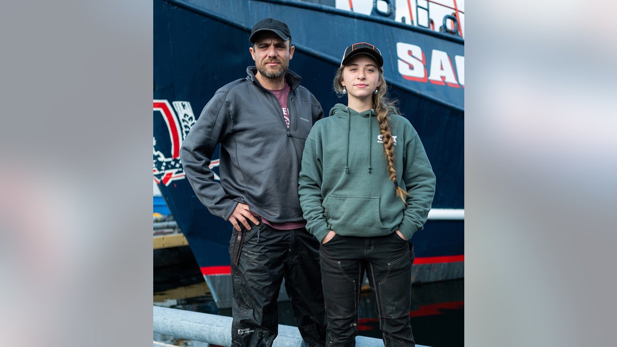 Jake Anderson and Sophia "Bob" Nielsen posing at the dock with the Saga in the background