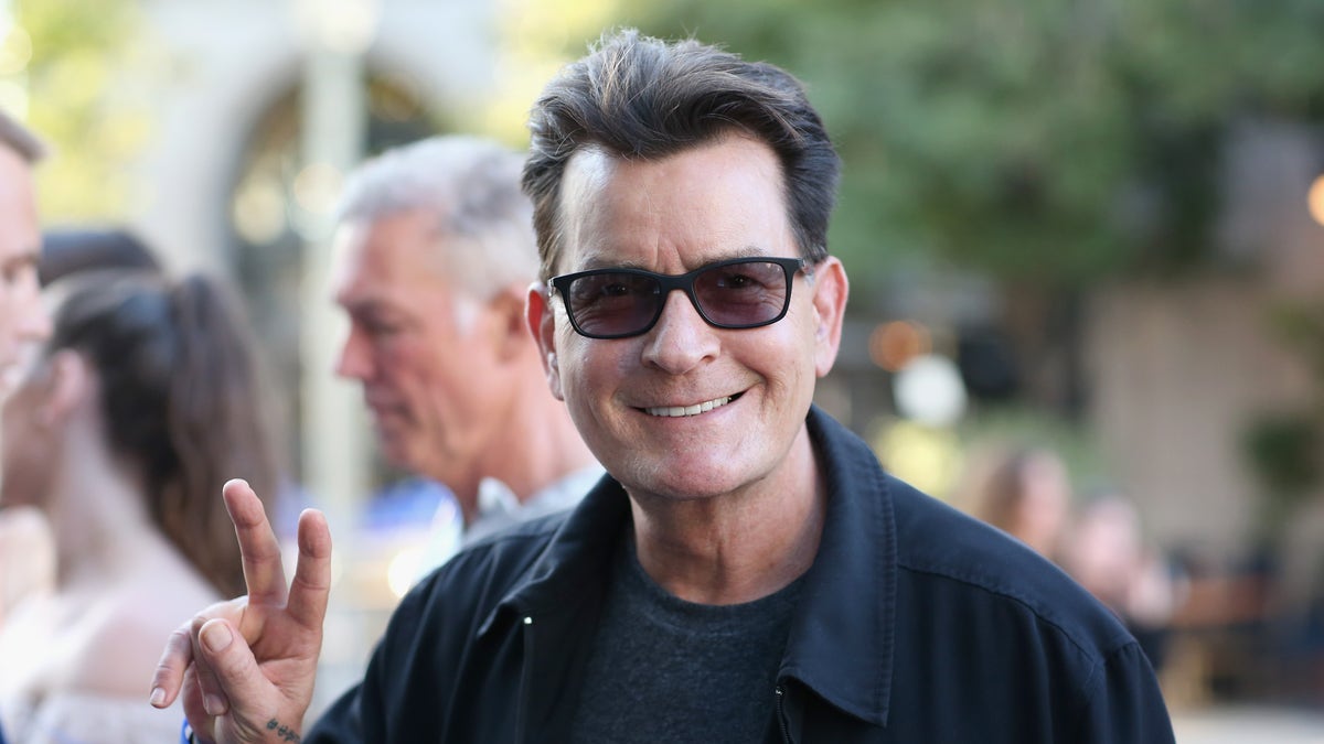 Charlie Sheen flashes a peace sign while wearing sunglasses.