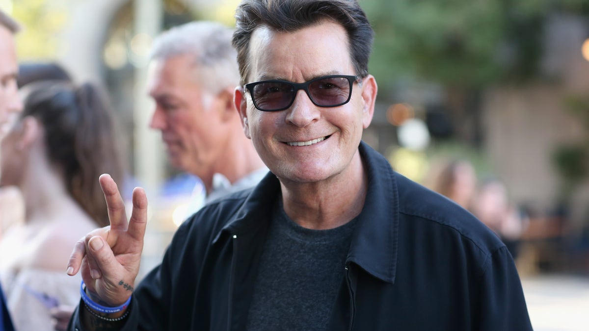 Charlie Sheen flashes a peace sign while wearing sunglasses.