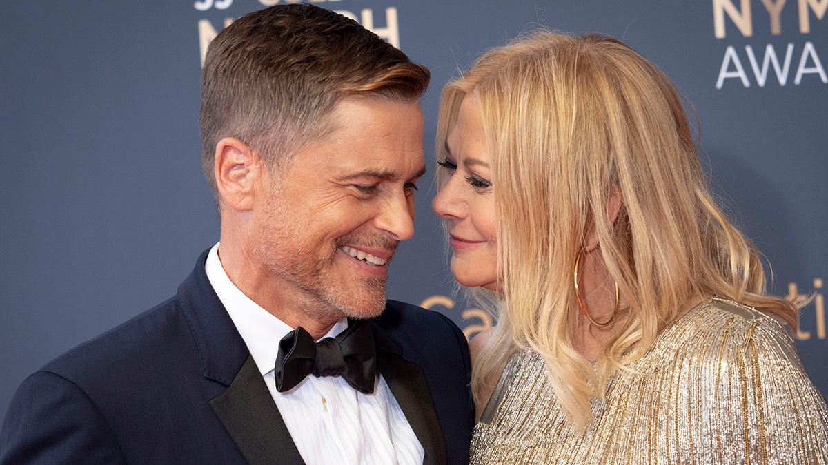 Rob Lowe in a navy tuxedo laughs as his wife Sheryl wears a gold sequin dress and looks lovingly at him on the red carpet in Monaco