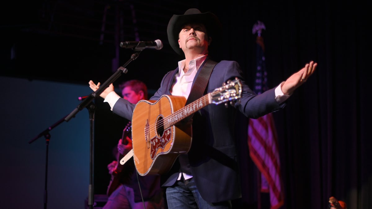 John Rich stands on stage with a guitar and cowboy hat