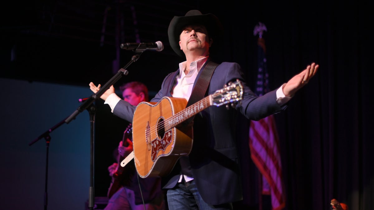 John Rich stands on stage with a guitar and cowboy hat