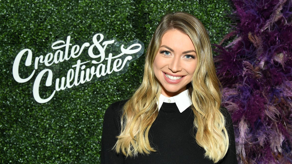Stassi Schroeder in a black sweater over a white collared shirt smilling