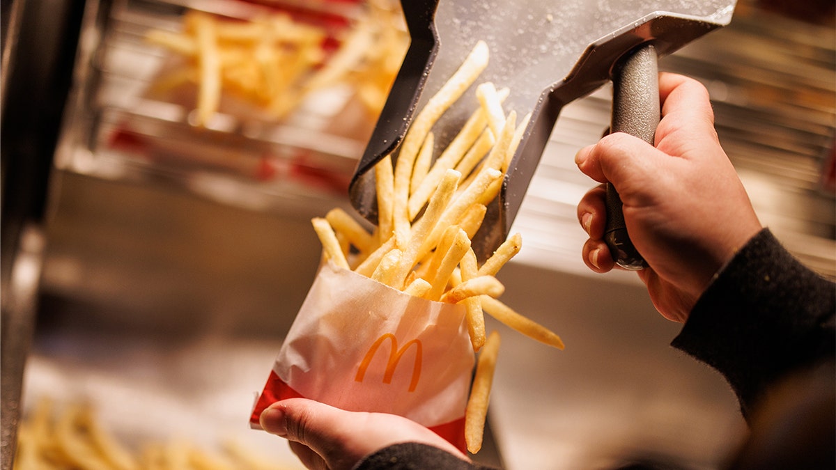 McDonald's kitchen employee shovels fries in small paper bag.
