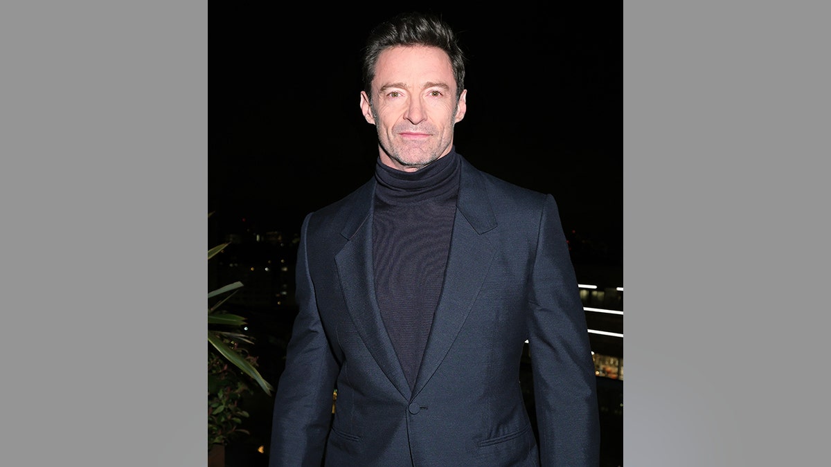 Hugh Jackman in a dark blue shirt and dark sea blue tight jacket on the red carpet in England