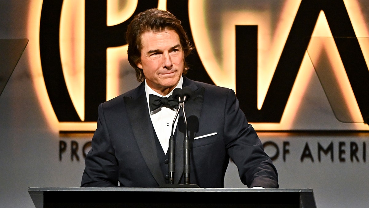 Tom Cruise on stage in a classic tuxedo behind the podium at the Producers Guild Awards