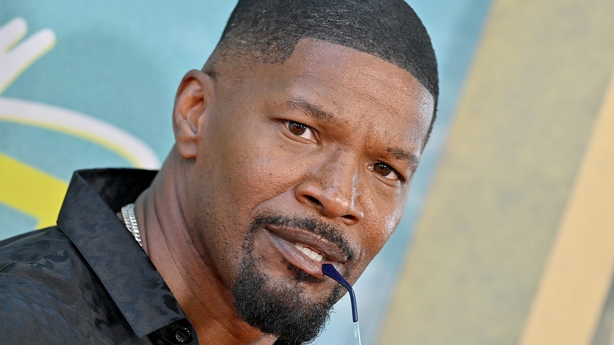 Jamie Foxx bites on his sunglasses ear piece while posing in front of the camera on the red carpet