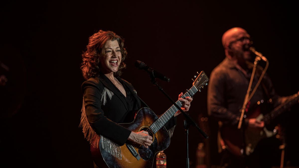 amy grant smiling while playing guitar on stage during tour