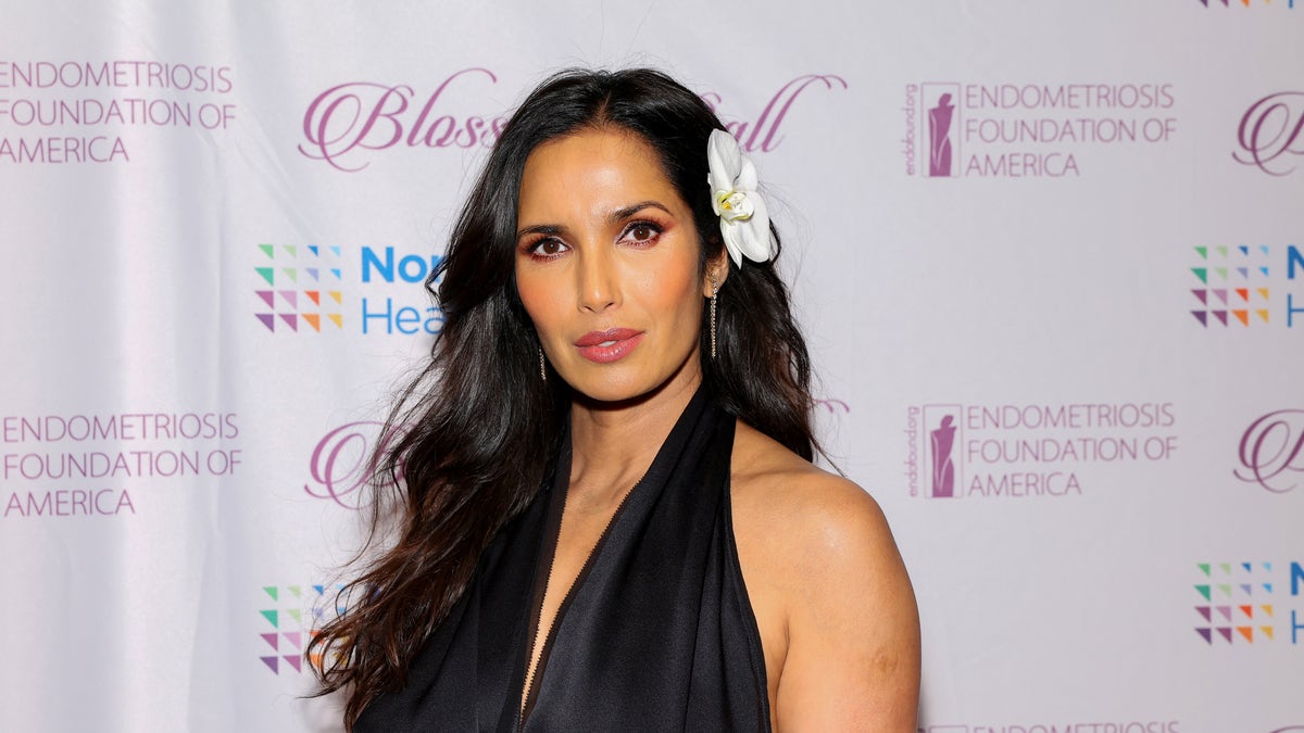 Padma Lakshmi wearing a v-neck black dress with a flower in her hair