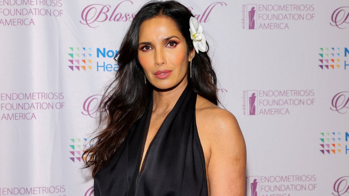 Padma Lakshmi wearing a v-neck black dress with a flower in her hair