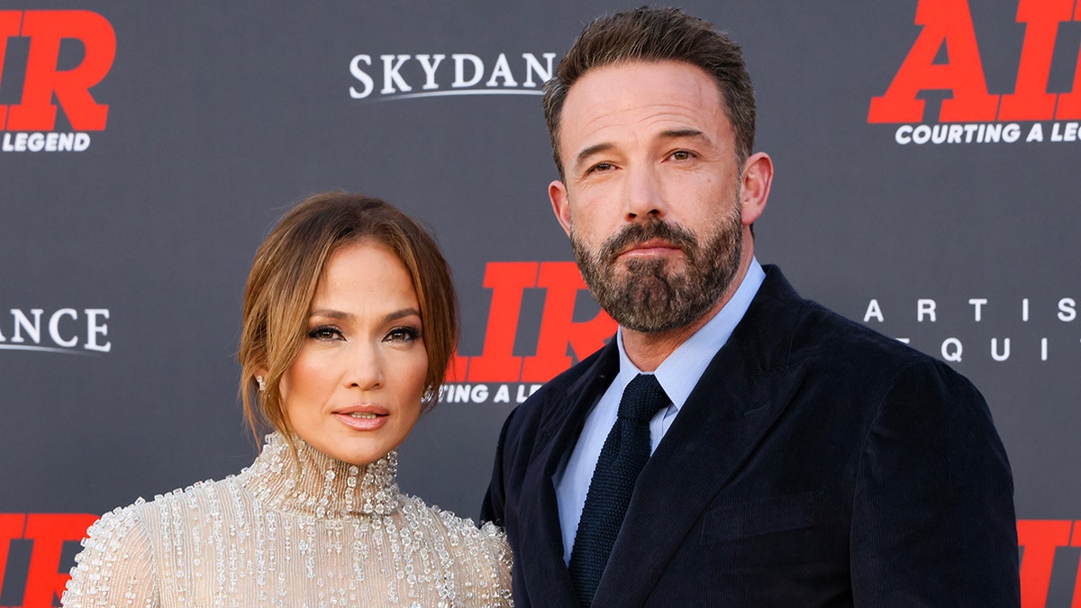 Jennifer Lopez smizes on the red carpet in a dress with a beaded transparent top next to Ben Affleck in a light blue shirt, black suit and tie on the red carpet for "Air"