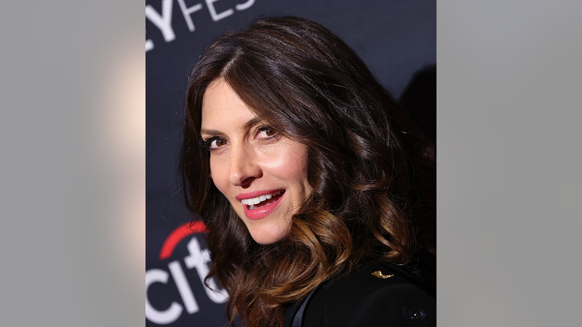 Dawn Olivieri looks back and smiles on the carpet at PaleyFest with voluminous brown waves