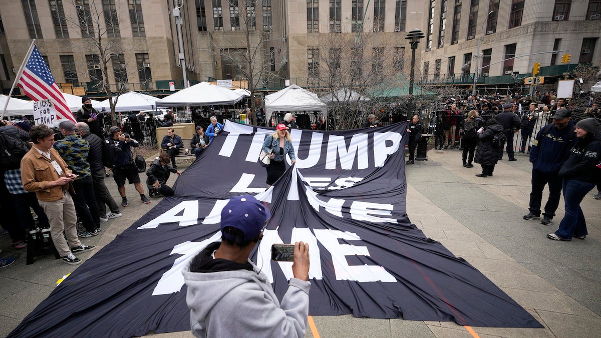 A supporter of former U.S. President Donald Trump stands on a banner criticizing him outside the courthouse where Trump will arrive later in the day for his arraignment on April 4, 2023 in New York City. With his indictment, Trump will become the first former U.S. president in history to be charged with a criminal offense. (Photo by Drew Angerer/Getty Images)