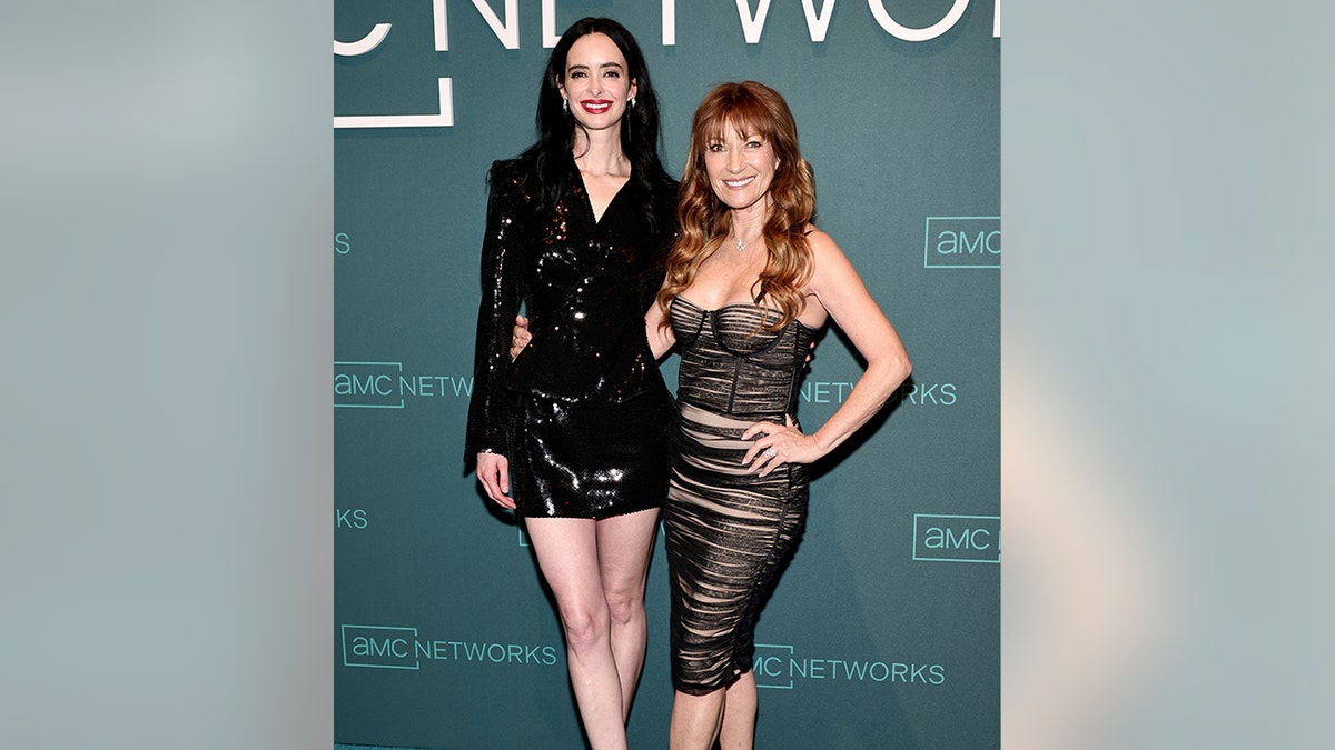 Krysten Ritter in a sparkly black peplum blazer and matching bottoms poses next to Jane Seymour in a ruched black dress on the AMC Upfront red carpet