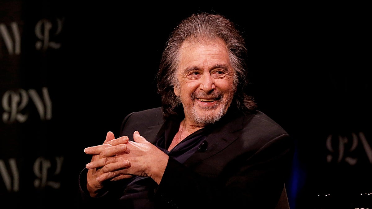 AL Pacino in a black suit on sitting in a chair on stage.