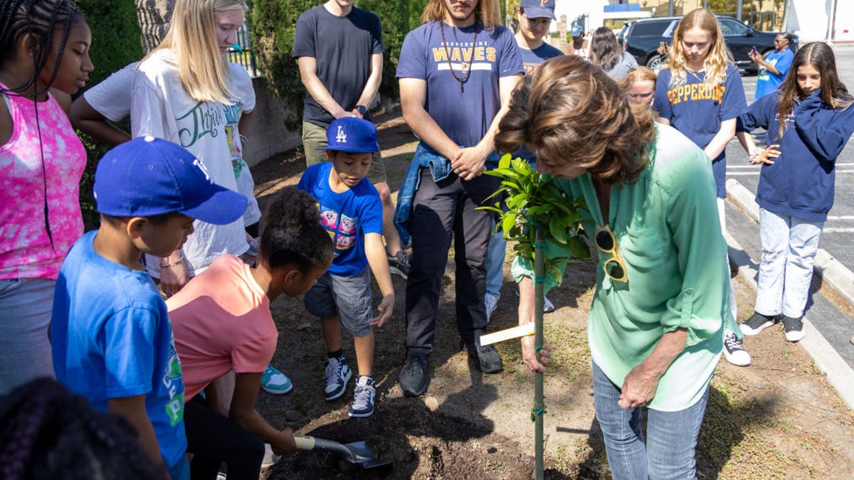 amy grant planting a tree while students watch