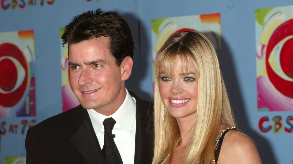 Charlie Sheen in a black suit and tie poses with Denise Richards in a black dress