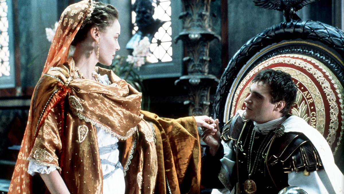 Joaquin Phoenix sits on a throne and holds the hand of Connie Nielsen in a scene from "Gladiator"