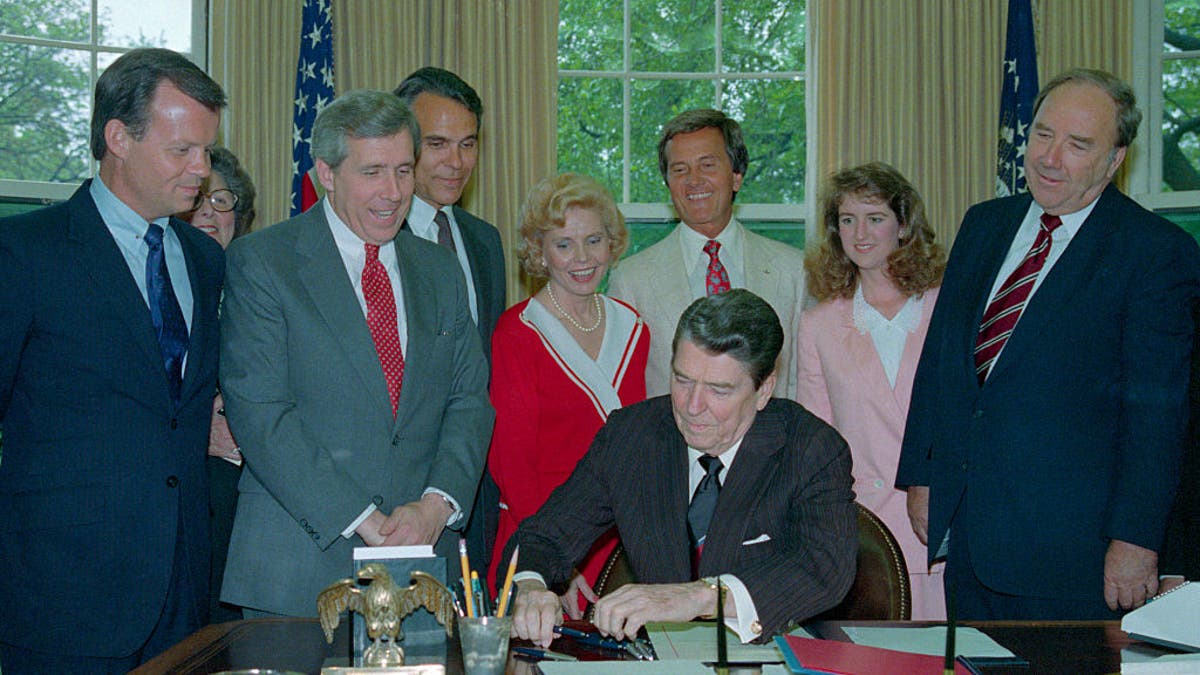 Members of the National day Prayer organizing committee looking on, including entertainer Pat Boone, (C-white suit), President Reagan signs a proclamation honoring the day in an oval office ceremony May 5th.