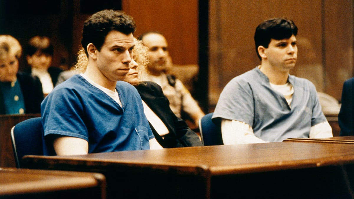 Menendez brothers Erik and Lyle sit behind a desk in court wearing blue prisoner garments