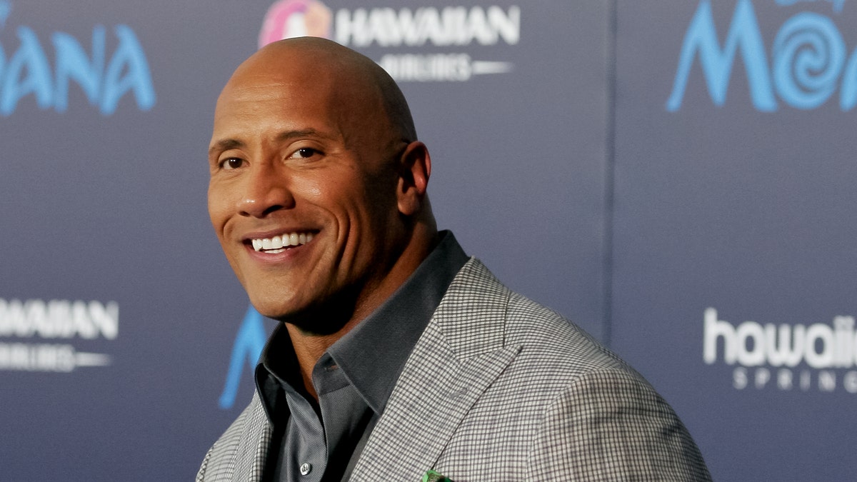 Dwayne 'The Rock" Johnson smiles in a grey checkered blazer on the carpet
