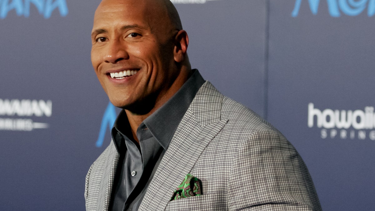 Dwayne 'The Rock" Johnson smiles in a grey checkered blazer on the carpet