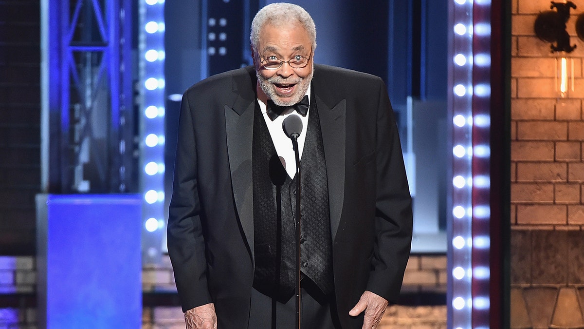 James Earl Jones hunches over slightly at the Tony Awards in a classic black tuxedo as he speaks into a microphone