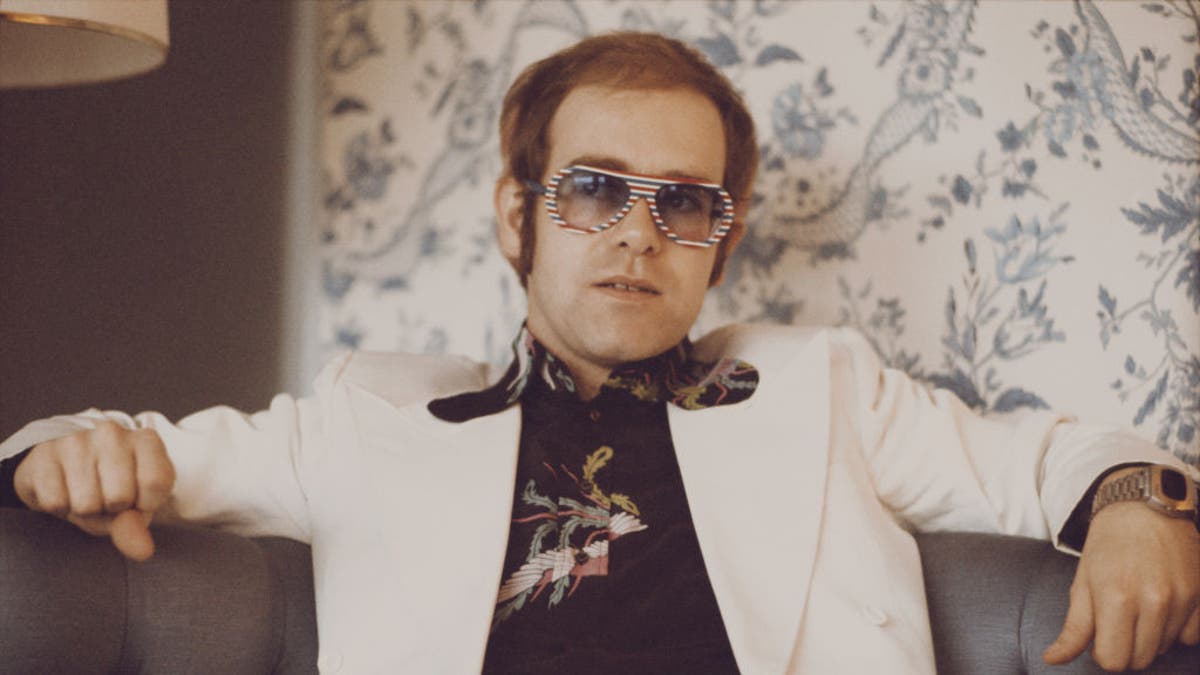 British singer and musician Elton John, wearing a white suit, black shirt with flower motif and multicolored sunglasses, London, November 1973